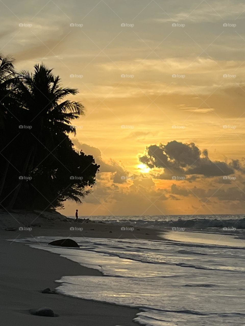An enchanting sunset on the southern island of Gnaviyani Fuvahmulah in the Maldives. Golden rays decorate the horizon while the sun bids goodbye from behind the clouds, and ripples crawl slowly on the beach. 