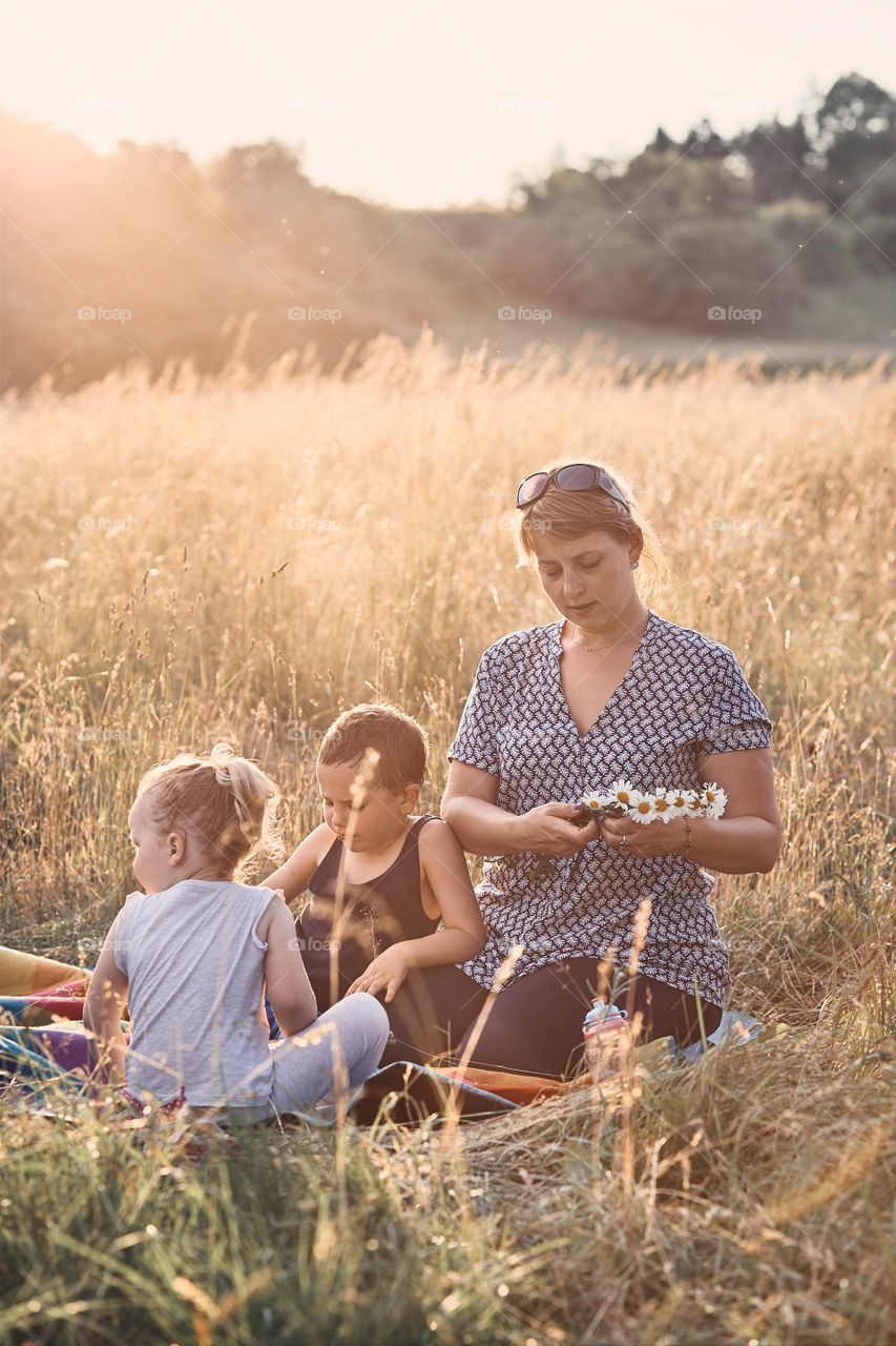 Family spending time together on a meadow, close to nature, parents and children playing together, making coronet of wild flowers. Candid people, real moments, authentic situations