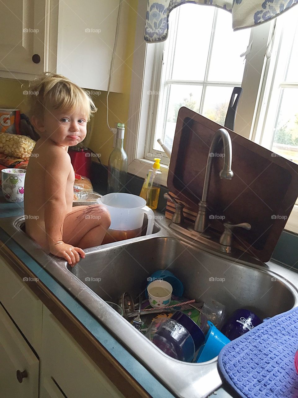 Naked little toddler that has climbed into the kitchen sink. 