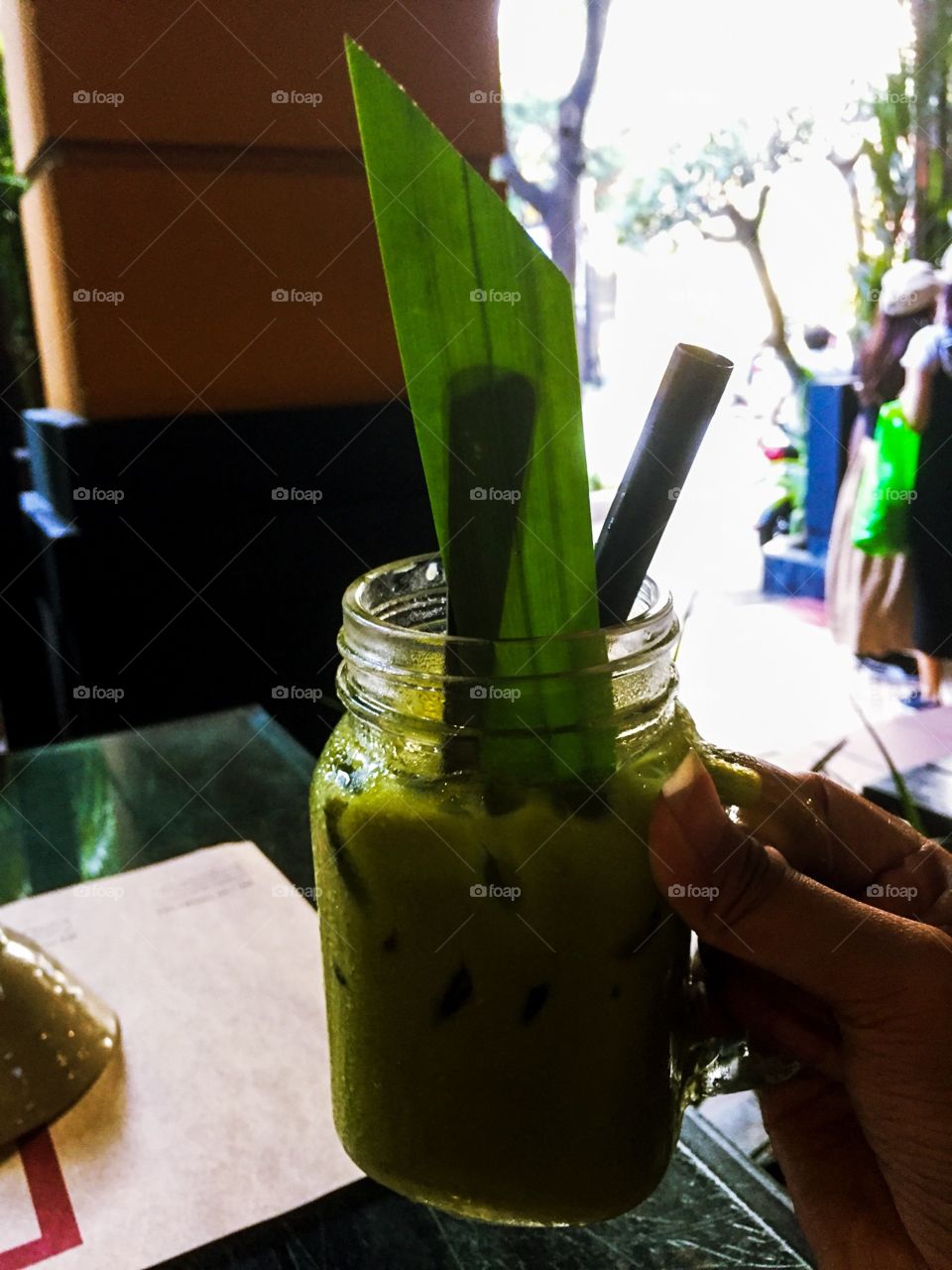 Hand holding a Thai cold tea glass , very beautiful green color. I am sitting in a restaurant for lunch