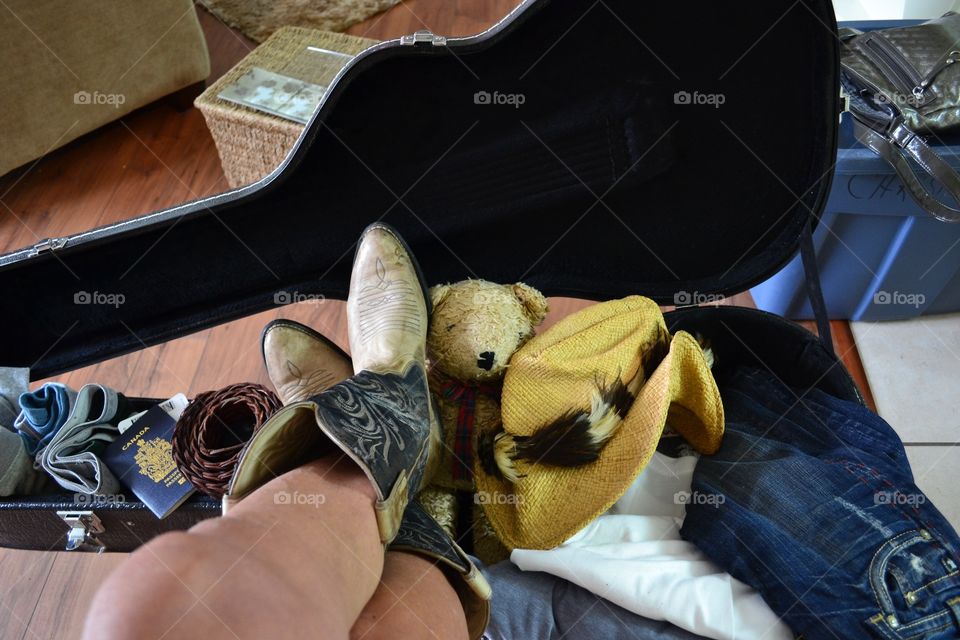 Country western woman in cowboy boots by guitar case serving as suitcase