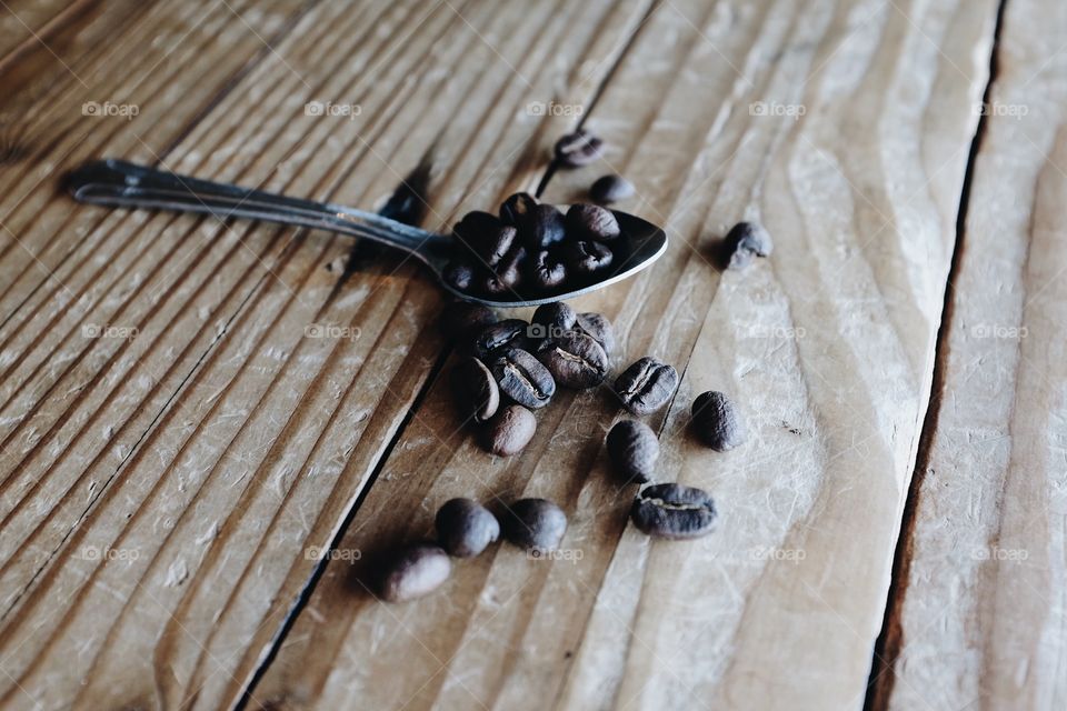 Coffee beans sitting on a small spoon with some natural light scattered across a table top. 