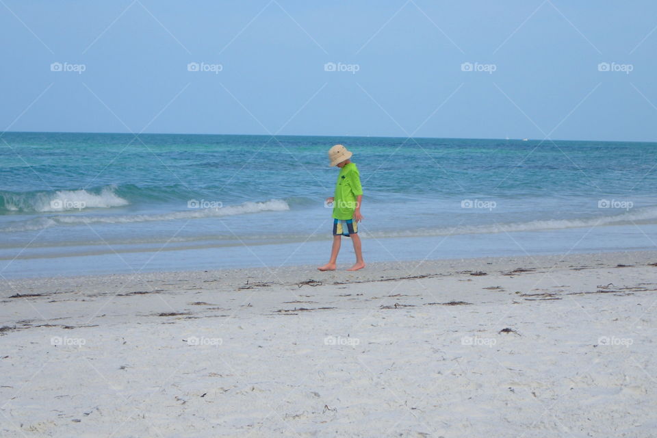 Young boy wearing hat looking for shells by shore of Gulf of Mexico