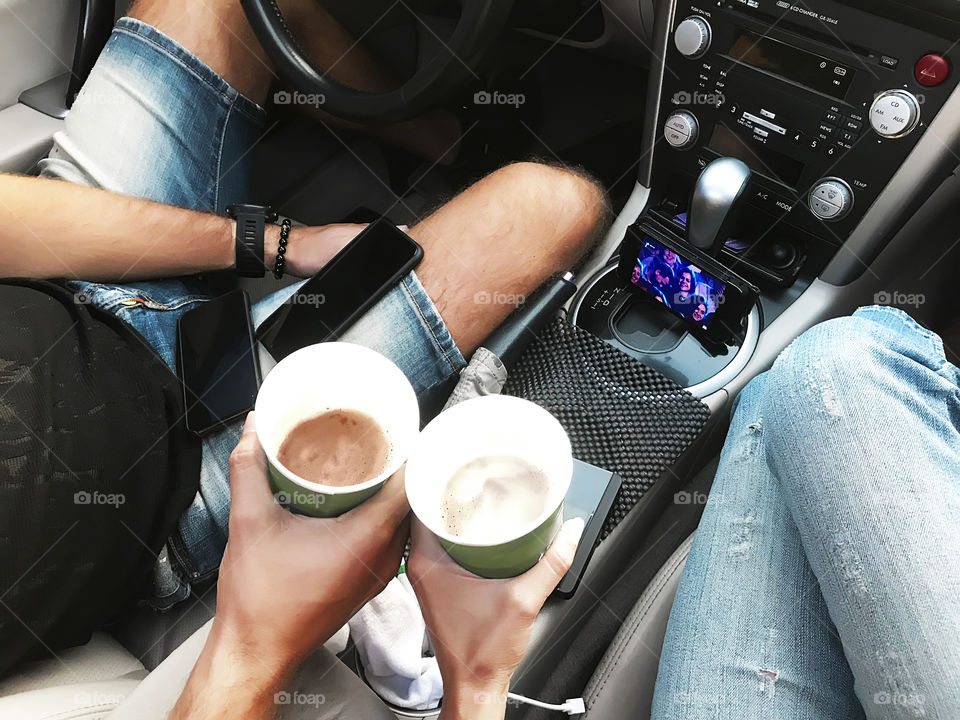 Young man and young woman drinking beer from the paper cup and enjoying funny video in the car