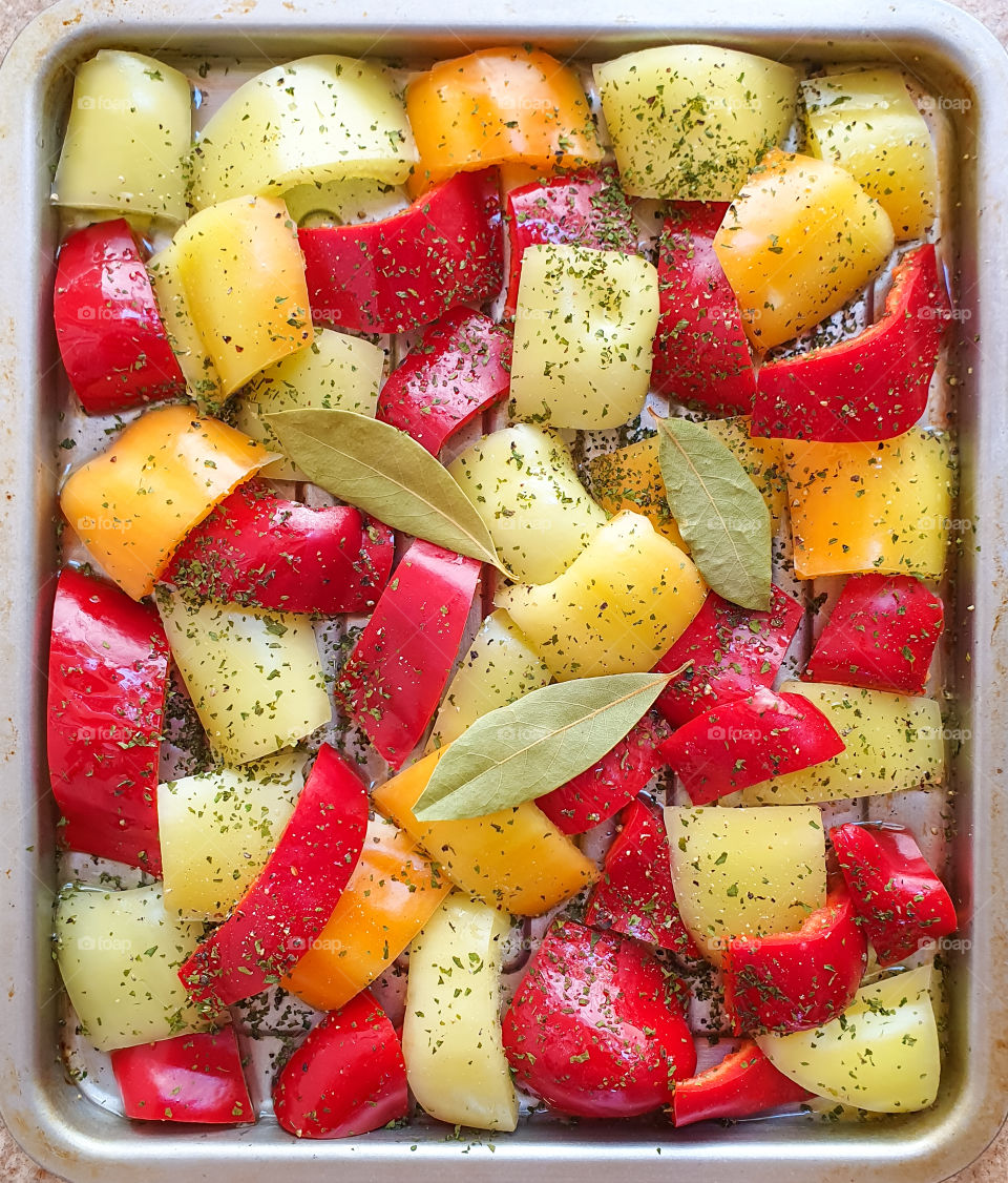 Fresh red, yellow, green bell pepper sliced in small pieces with spices and bay leaves on a baking sheet and ready for cooking, baking. Healthy, vegetarian food. Paprikash