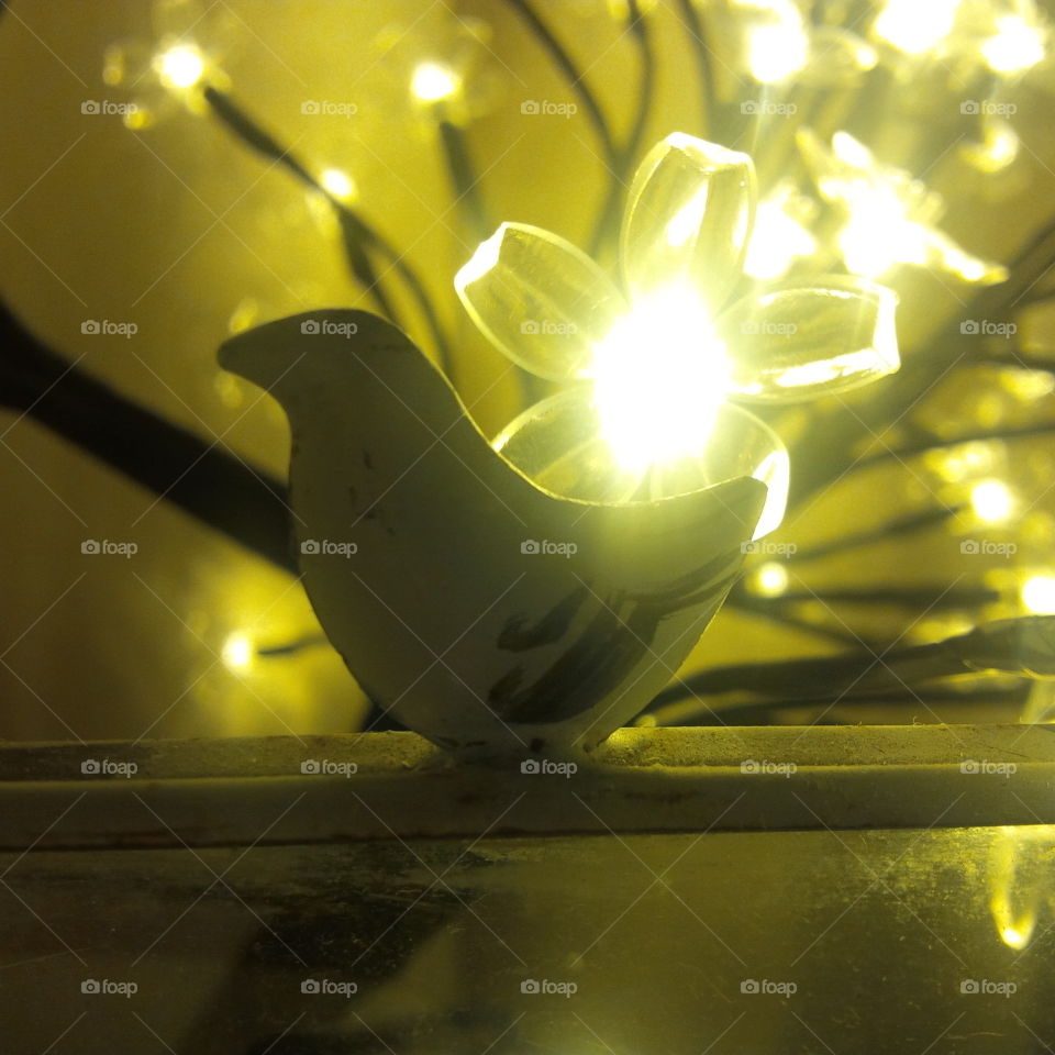 yellow toned flower fairy lights with a little ornate bird in front of them.