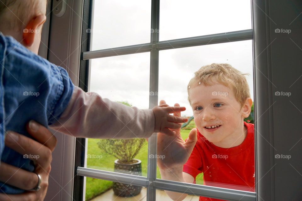 Brother and sister touch hands through a glass window 