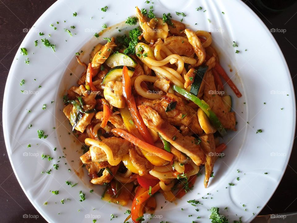 a delicious portrait of a tasty dish of noodles with chicken in a white plate in a restaurant.