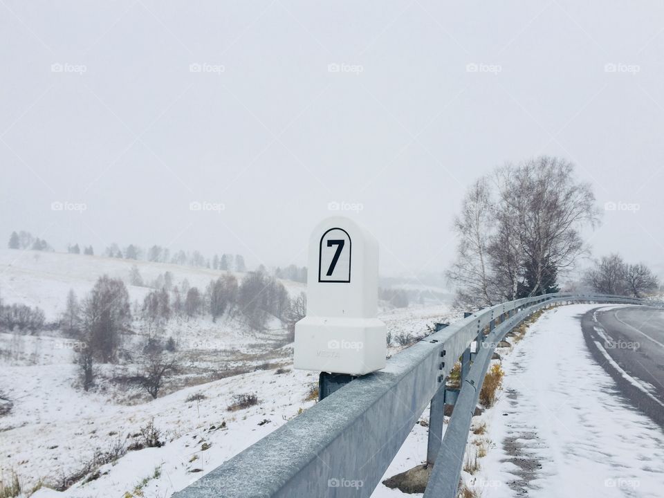 Stone mileage sign on a deserted road covered in snow during winter