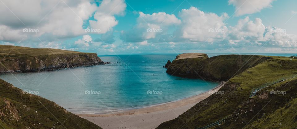 A high angle shot of the beautiful sea surrounded by green hills under the cloudy sky during daytime