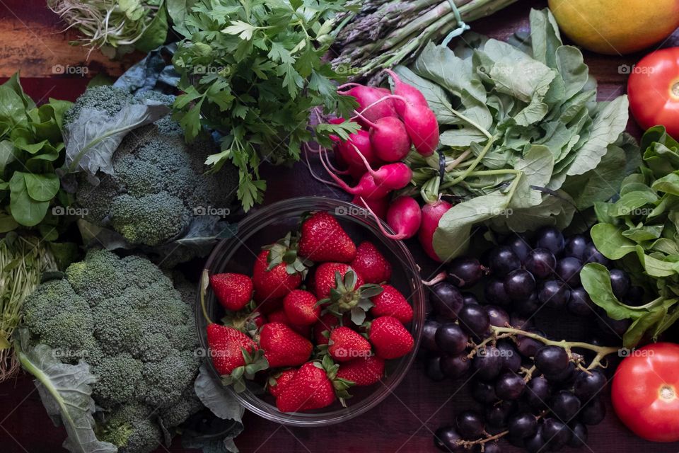 A wooden table full of organic vegetables, herbs, berries and fruits. Flat lay with strawberry, broсcoli, arugula, tomatoes, mango, cilantro, grape, radish. Farm fair products