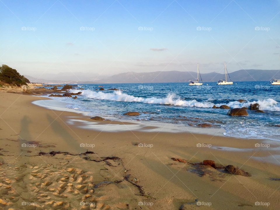 Golden sandy beach, foamy waves and sailboats in the background at sunset, Porto Pollo, Corse, France