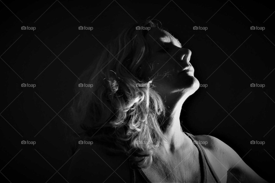 black and white low key self portrait woman with curly blond hair seen from the side against a black background