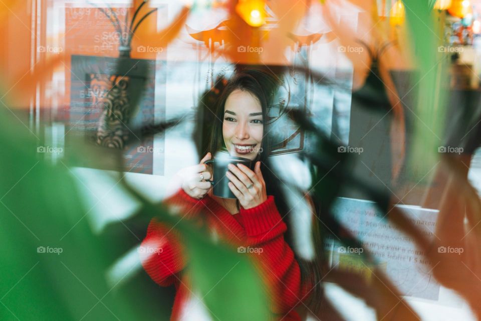 Beautiful smiling young asian woman in red with cup of tea restaurant through window