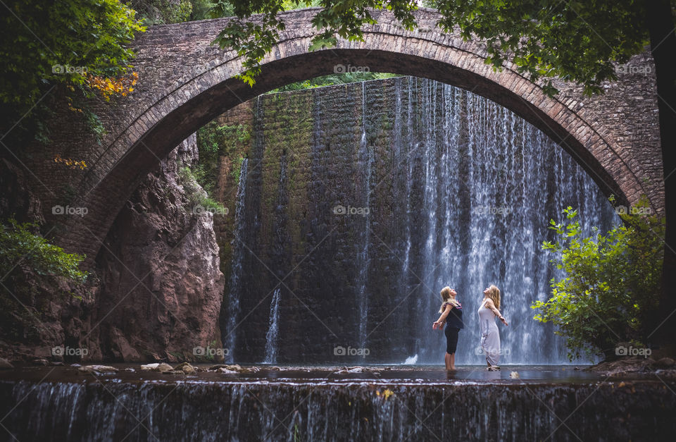 Two women enjoying nature in Palaiokarya dam, bridge and waterfall in Thessaly, Greece.