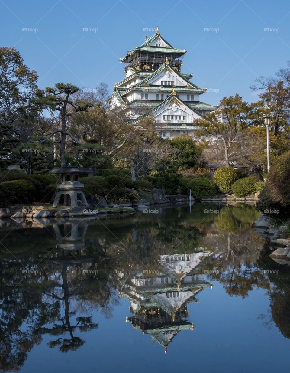 Japanese castle reflecting in a pond with a bright blue sky