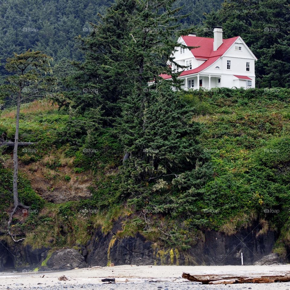 A big two story White House with red roof perched on a cliff in the hills above the Pacific Ocean in the Central Oregon Coast on a fall day. 