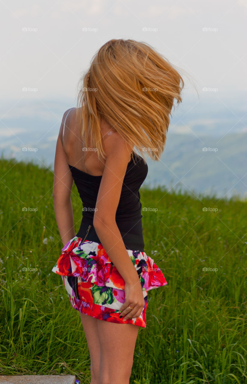 Rear view of blonde woman standing near green field