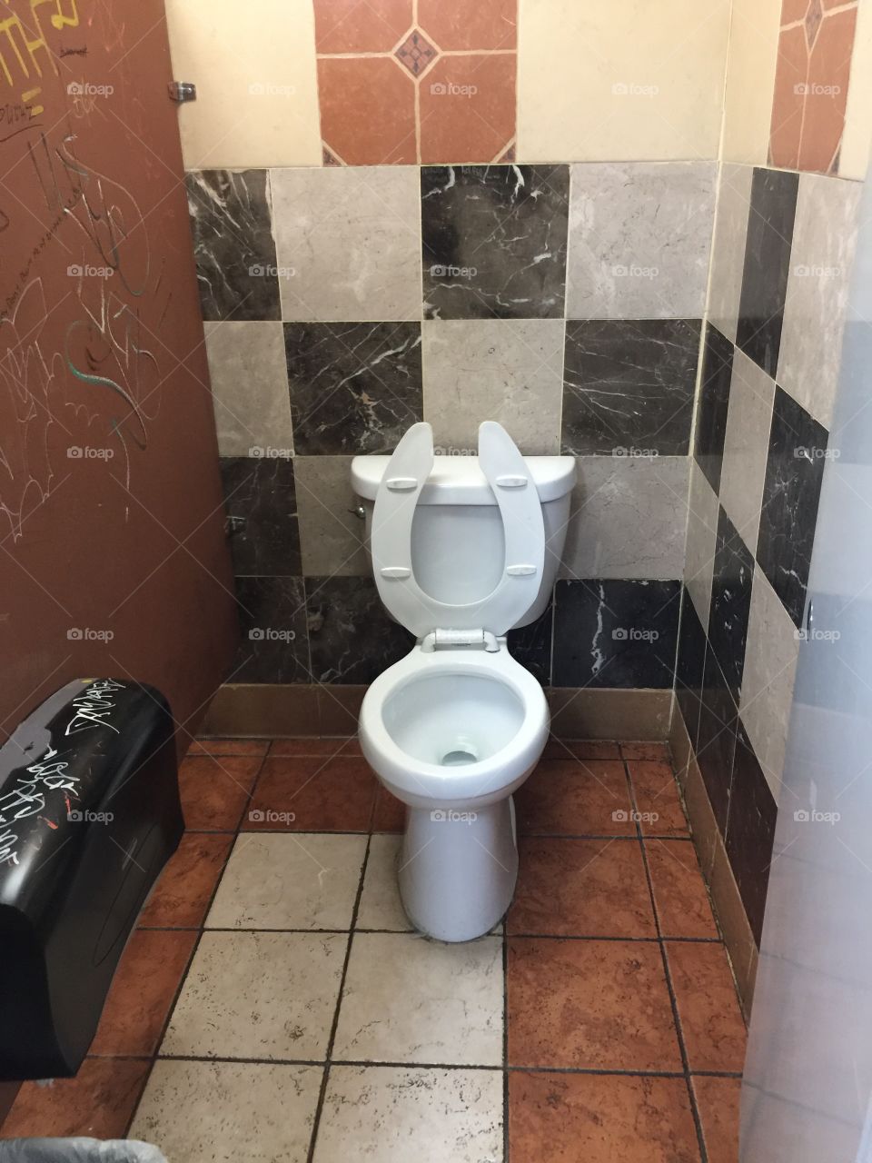 A men's room toilet with graffiti and tile flooring.