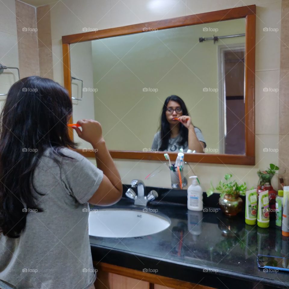 young woman brushing her teeth looking at the mirror at home