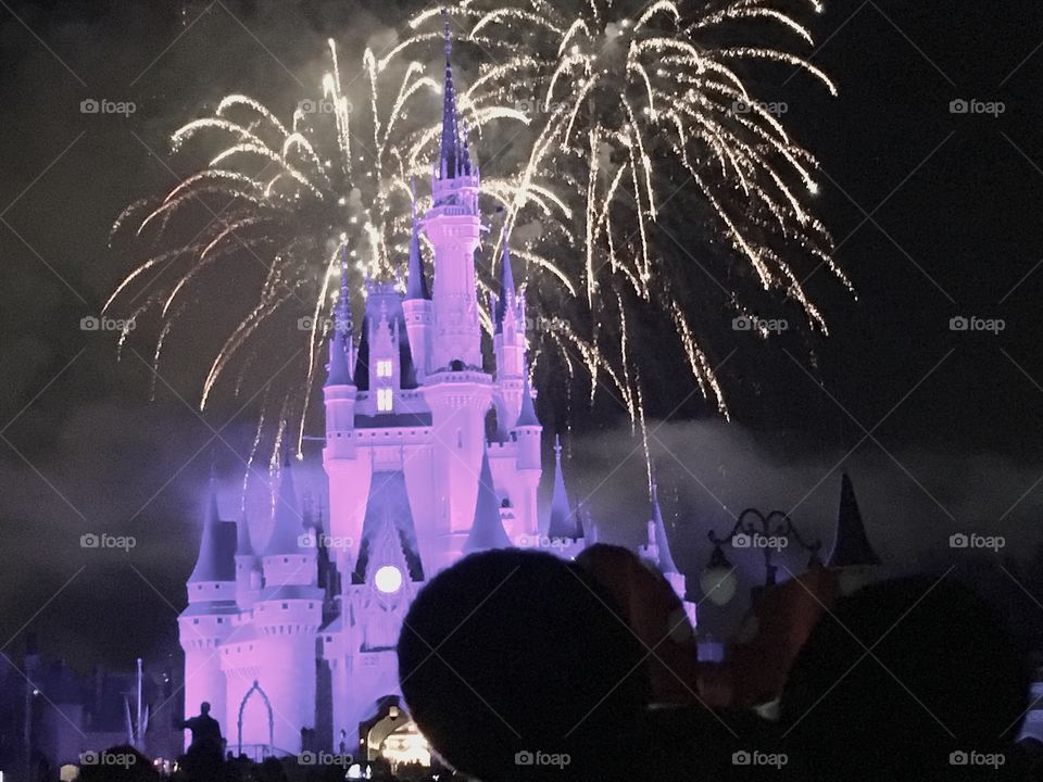 Fireworks over Cinderella’s Castle in Disney World with someone wearing Minnie Mouse ears 