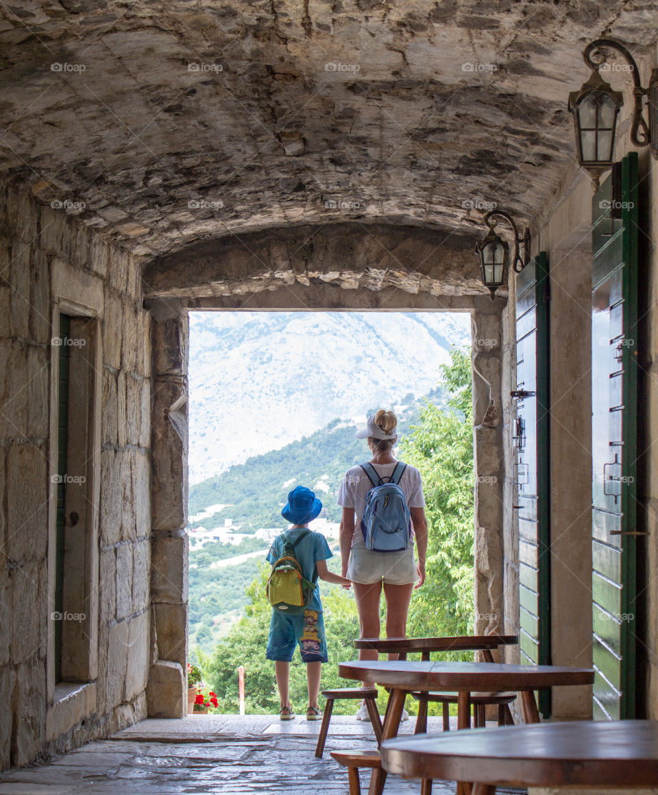 Summer landscape with historic building and mother and son. Woman with child holding hands standing in the arch of an old brick bastion and looking at a beautiful Mediterranean landscape.