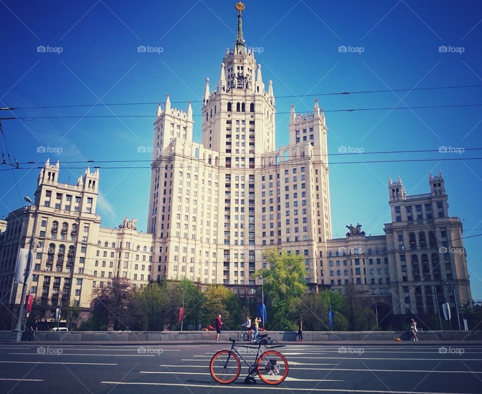 Grey brakeless fixie bike with orange wheels in front of Moscow soviet Stalin skyscraper, Russia 