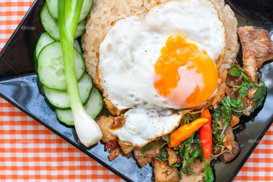 Pork with chilli & Basil leaves topping with fried egg on plate.