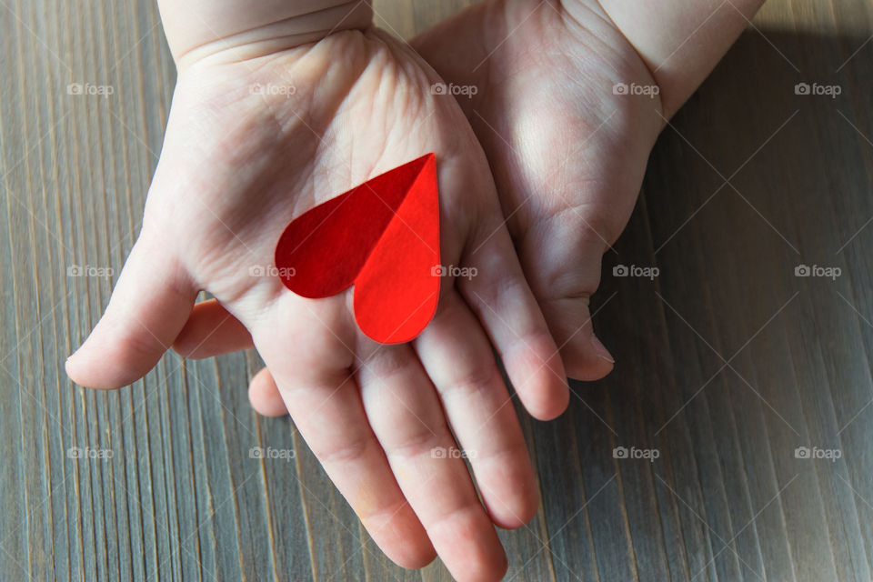 Red paper handmade hearts in child hands on the wood background. A gift for Valentines Day and Mother Day.