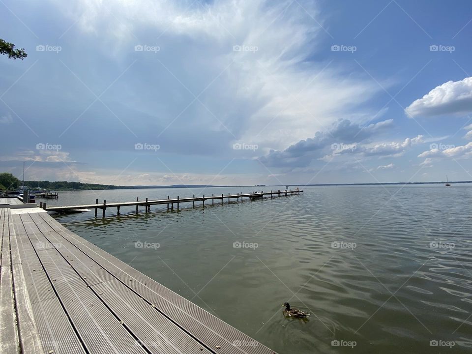 L-förmiger Steg am Steinhuder Meer in der Abenddämmerung bei mit Schlierwolken behangenem Himmel. Eine Ente schwimmt im unteren Bildrand. Der Sonnenuntergang ist am Horizont noch zu erahnen.