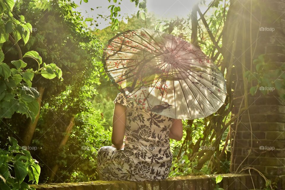 Rear view of woman holding a Chinese paper parasol in garden.