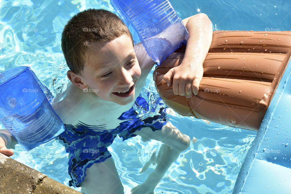 A Young Boy Playing In The Swimming Pool With Floatation Device In The Summer