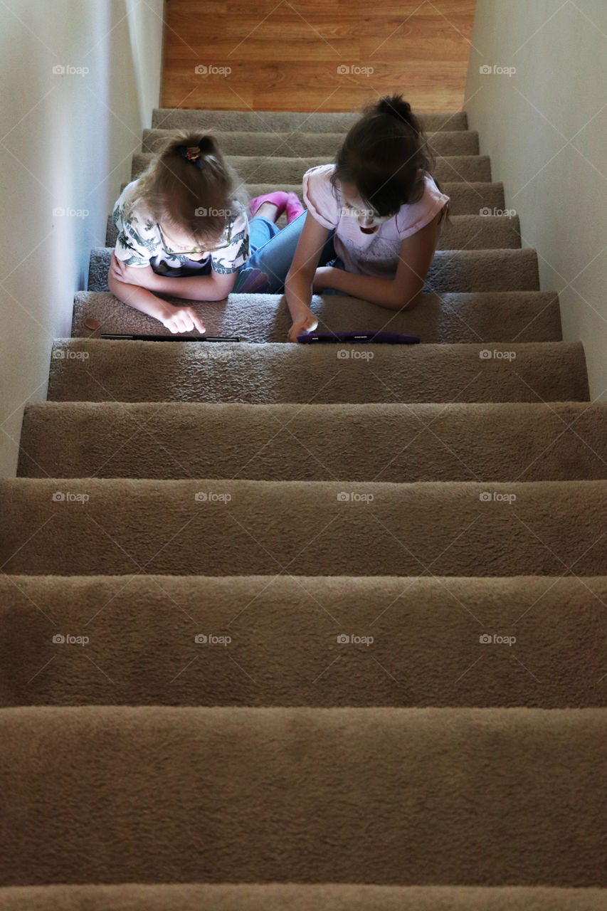 Sisters sitting on the stairs while playing on their tablets