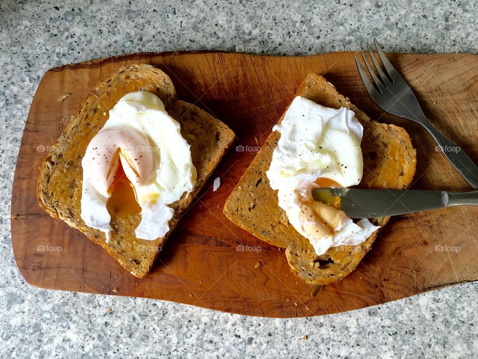 Poached eggs on toast on olive wood with cutlery 