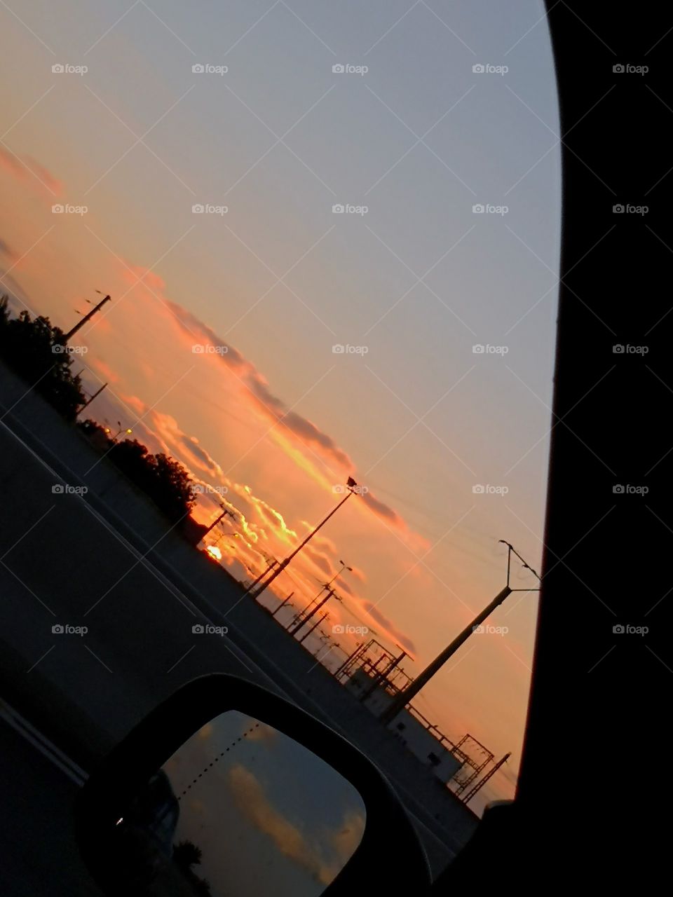 orange sunset with wavy pink clouds over side mirror of a car