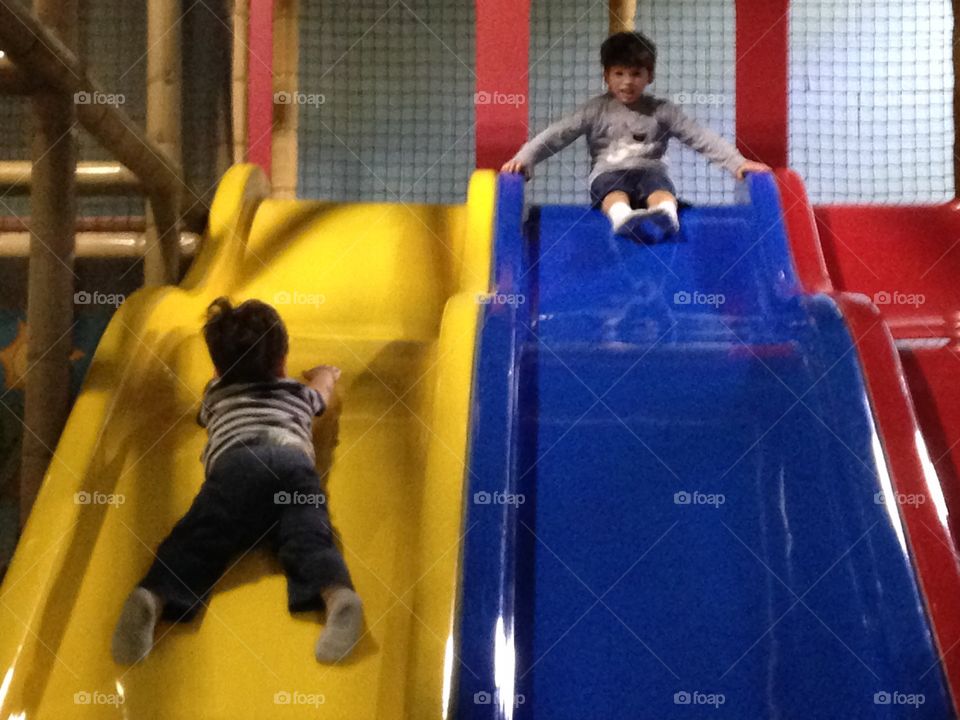 Two boys sliding indoors at an indoor playground.