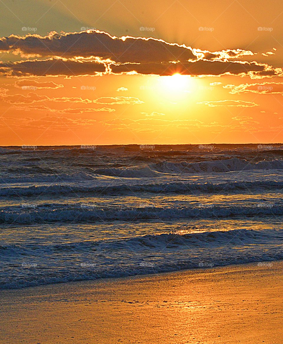 Sunset over the Gulf of Mexico - sun reflected waves crash the sandy beach as the clouds captures the results of a spectacular sunset