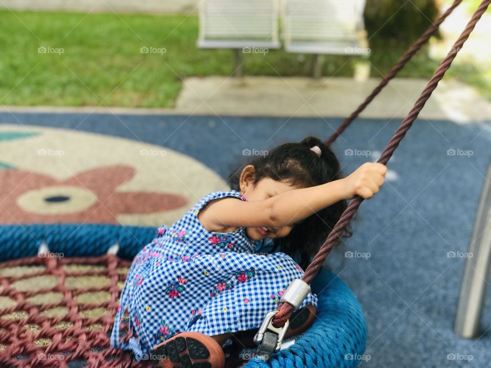 A girl swinging on the round shape swing and smiling.