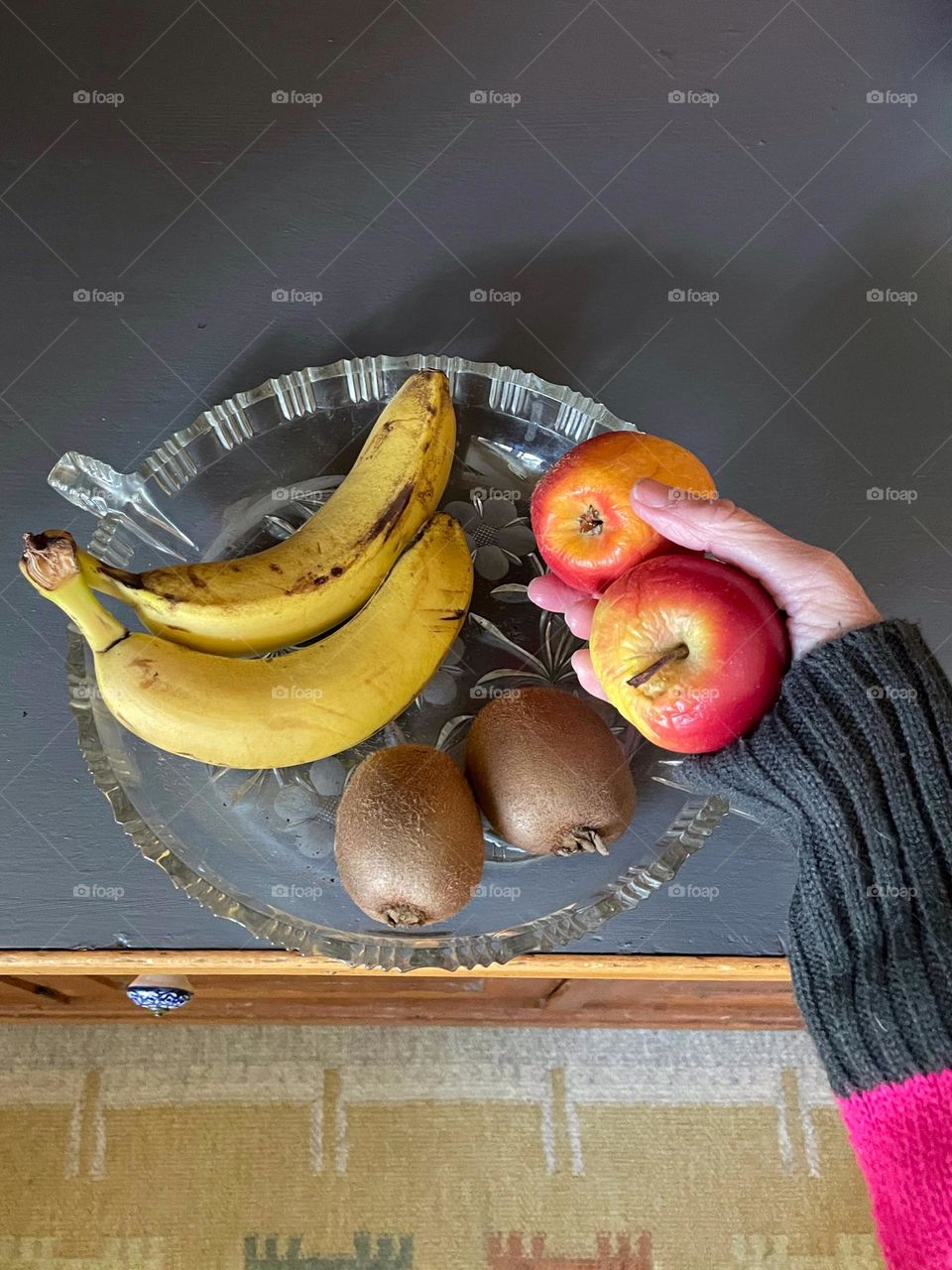 Top view of a fruit bowl and a hand putting apples in it