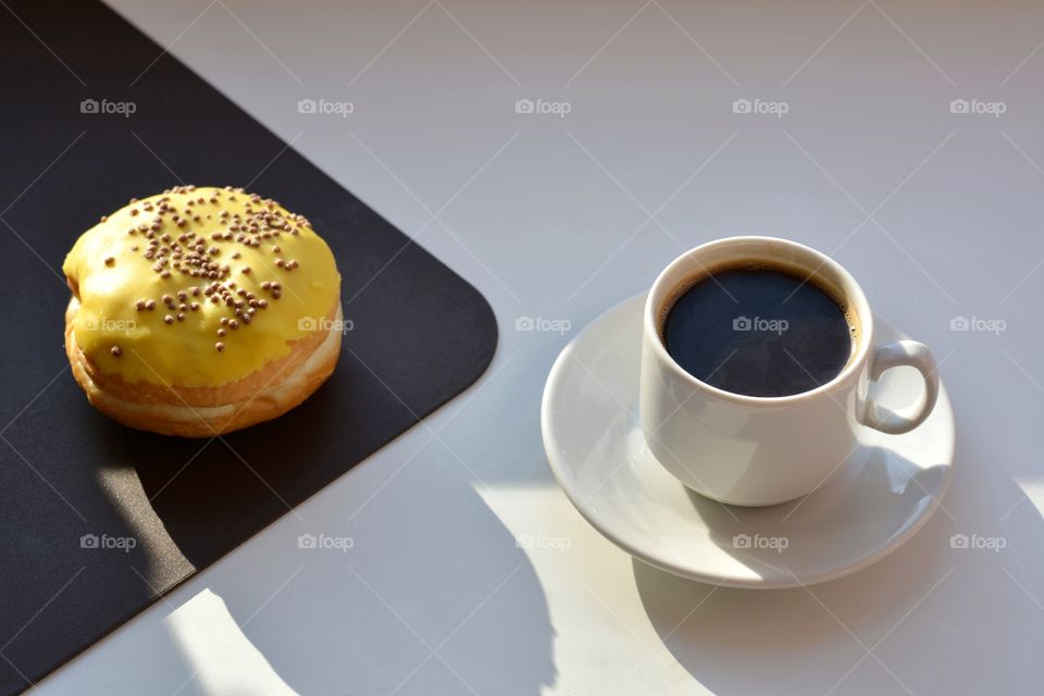 cup of coffee and bun sweet in sunlight and shadows on a white and brown background, morning routine