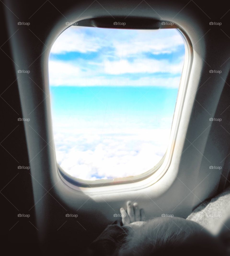 A baby looking out the window of his very first airplane ride. Enjoying the beautiful blue sky.