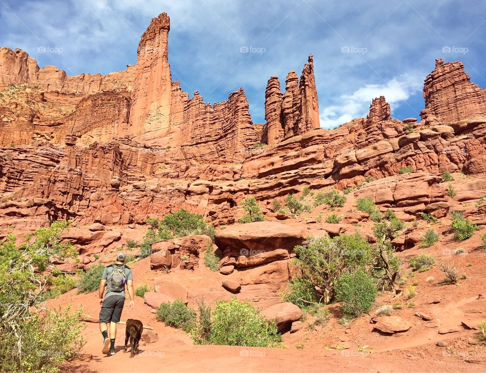 A man and his dog hiking the Fischer Towers trail in Moab, Utah on a beautiful spring day. 