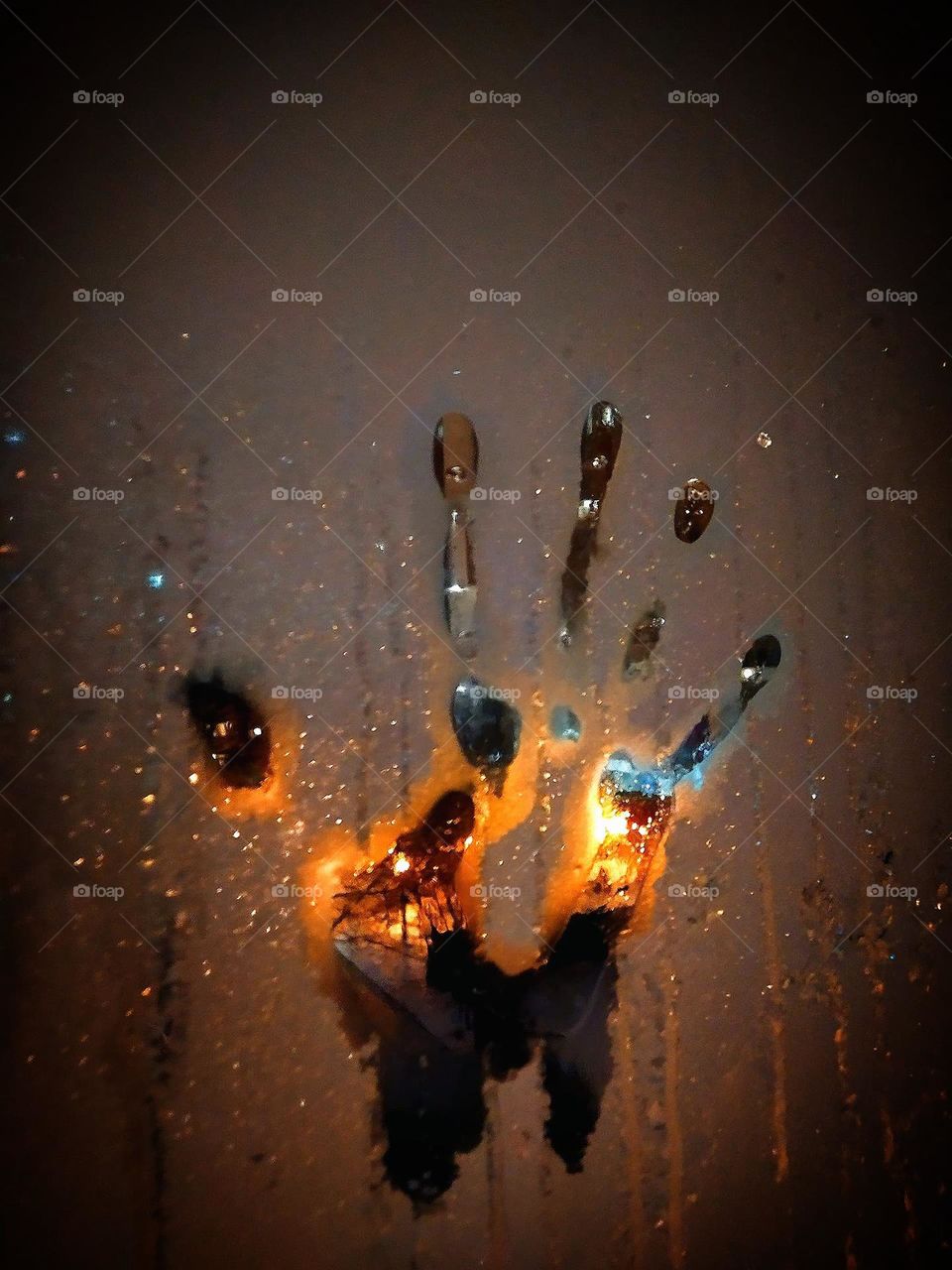 There is a handprint on a window covered with frost. Street lamps give magical colors handprint