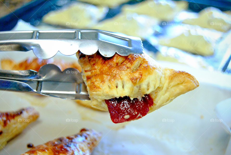 homemade glazed guava cheese strudel held in a thong, after baking, front focus, guava oozing out