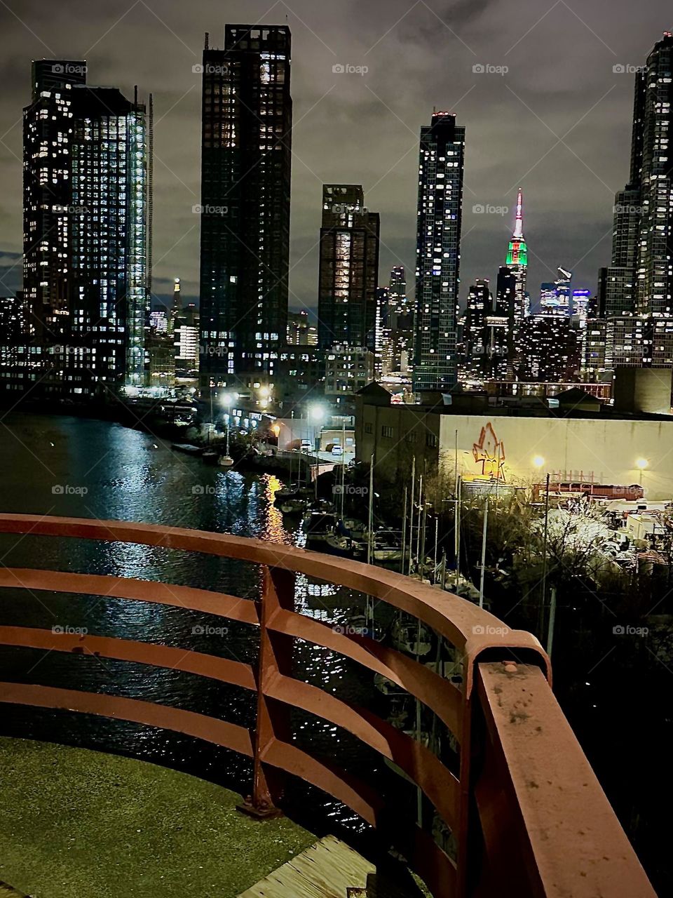 This is “Newtown Creek” at nighttime seen from the “Pulaski Bridge” that connects “Greenpoint”, Brooklyn to LIC, Queens. In the distance we see “Manhattan” incl. the “Empire State Bldg” illuminated in red, white and green. 2023. Hypnotic Productions