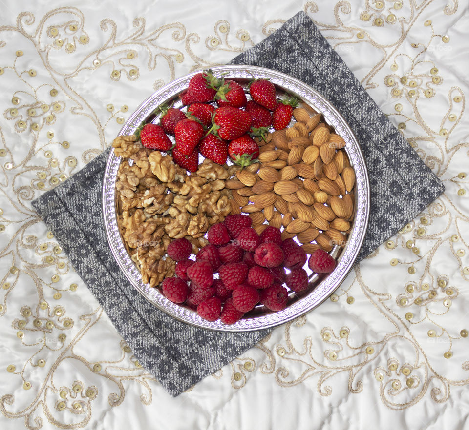 Berries and nuts on a silver tray on embroidered ornamental napkins. Healthy food