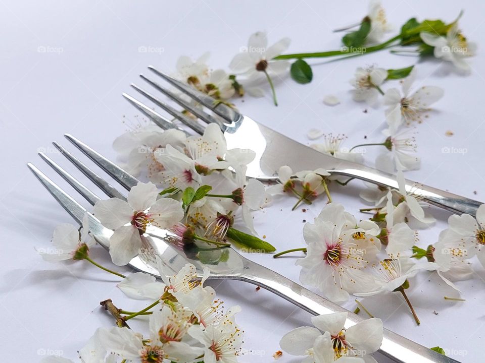 Two metal forks on the white table decorated with white flowers