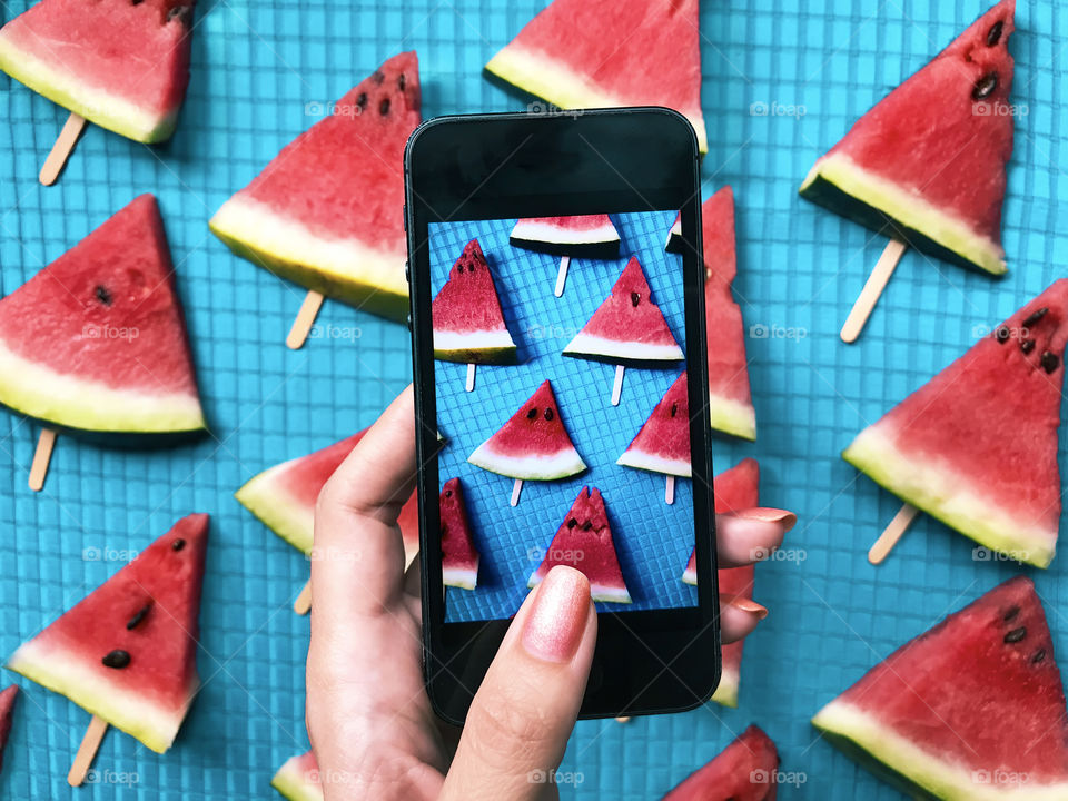 Female hand taking a photo of slices of red ripe watermelon 