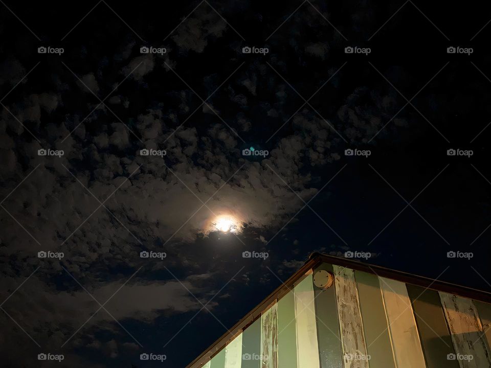 Strong Cold Light From The Moon And The Moonbeam Above The Top Of The House With A Halo Of Light And Colors Surrounded With Clouds.