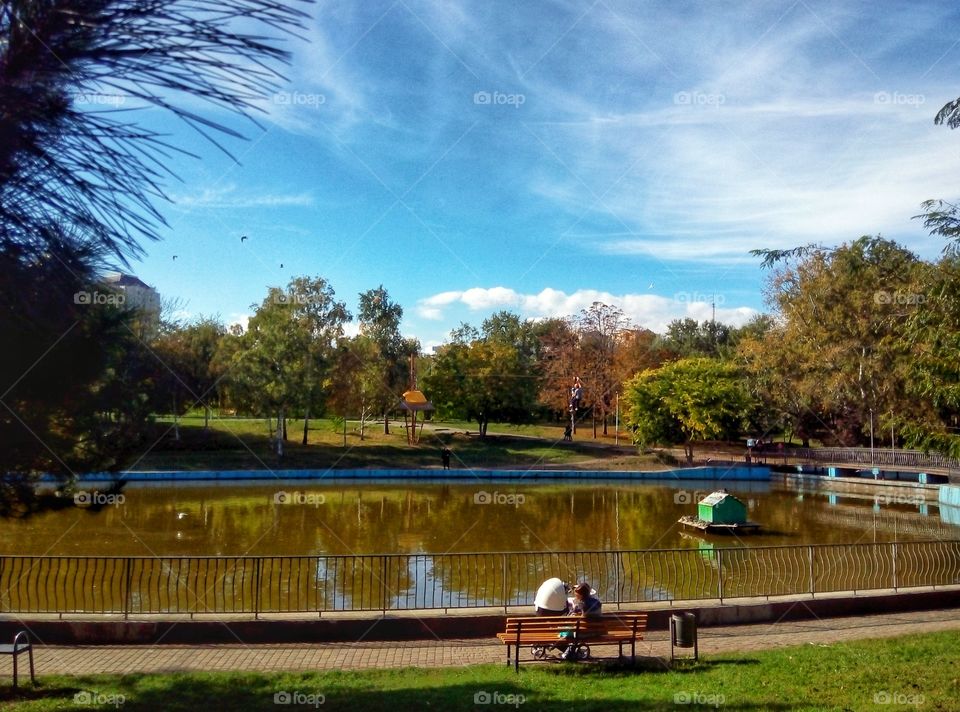 A young mother with a stroller on a bench by the lake молодая мама с коляской на скамейке у озера